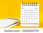 May 2023 Monthly desk calendar for 2023 year and calculator with pen on yellow background.