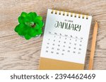 Small photo of January 2024 monthly desk calendar and pencil with plant pot decoration on wooden background.