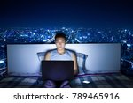 Attractive Asian man using laptop computer on his bed at night doing hard work and blue light reflection from computer screen