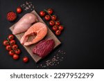 Chicken or turkey fillet, raw beef steak and salmon steak with spices and herbs on a dark concrete background