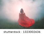 Small photo of gorgeous amazing wonderful scarlet red dress with a long flying waving train, a mysterious girl with red curly hair runs away into a thick white mist and forest haze over the green summer grass