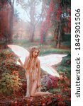 Small photo of Young beautiful fantasy woman in the image of fairy. Forest pixie girl with golden glowing butterfly wings. Fashion model posing in forest dressed as an angel. Bright colorful autumn foliage of trees