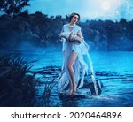 Fantasy woman Greek goddess zodiac sign Aquarius holds vintage earthenware jug in her hands and pours water into river. Background lake blue water, magic night, moon light stars. Astrology concept