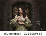 Small photo of Fantasy portrait woman princess keeps secret holds old key to all doors in hands. Background old wall, wooden door. Medieval Girl Vintage Golden Ancient Style Dress. keys fall hovering floating in air