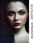Small photo of Gothic portrait of young green-eyed girl with black curles, black wings and brown smoky eyes and bardic lipstick with head down, eyebrow up and looking at you and smiling with eyes on black background