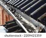 Small photo of Roof gutter cleaning. A clogged rain gutter of an asbestos roof with non flowing water from melted snow because of unclean gutters with dirt and fallen leaves. Rain gutter before cleaning.