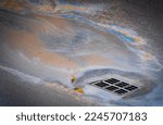Small photo of Oil slick on the asphalt road background drains into the storm drain. Water pollution environmental problems. Selective focus.
