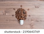 Small photo of Glowing light bulb shape made from coffee beans and a cap on a wooden table. Brain activity stimulus concept.