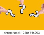 Small photo of Close-up view of three white and black plastic question marks in hands isolated on plain yellow background with copy space. The concept of curiosity, inquiry and the search for answers.