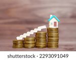 Small photo of Colorful toy house figure and a miniature staircase resting on top of a pile of coins, all set against a wooden background. Home owning dream, mortgage and investment related concept.