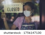 Close up shot of woman wearing mask and hand turning closed sign board on glass door in coffee shop and restaurant after coronavirus lockdown quarantine.Business crisis concept.