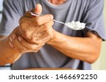 Elderly man is holding his hand while eating because Parkinson's disease.Tremor is most symptom and make a trouble for doing activities such as eat.Health care or elderly concept.Selective focus.