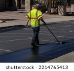 Small photo of Worker using a sealcoating brush during asphalt resurfacing project