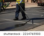Small photo of Worker spraying slurry tar on street during resurfacing project