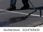 Small photo of Worker spraying slurry tar on street during resurfacing project