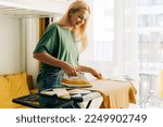Middle-aged woman housewife ironing clothes at home.