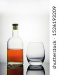 Small photo of a beautiful glass bottle of cognac or whiskey on a well-lit background stands next to a cognac glass. boredom and propensity to alcoholism, complete loneliness