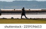 Small photo of Mid aged women walking along Everett, Washington's waterfront located at Boxcar Park. Bright natural sunlight beams "Possession Sound" behind and horizon landscape. Captured January 17, 2023.