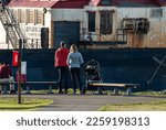 Small photo of Male and Female with baby stroller observe old rusty industrial boat with excavator full of water in background located at "Boxcar Park" in Everett, Washington's waterfront. Captured January 9, 2023