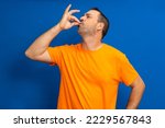Small photo of Portrait of a bearded hispanic man in orange t-shirt with puckered lips showing gourmet sign with fingers tasty delicious isolated on vibrant blue color background.