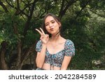 Small photo of A cute and sprightly asian woman in a fashionable crop top doing a peace sign. Outdoor scene.