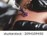 Small photo of A professional tattoo artist uses a rotary tattoo machine to shade a small flower. Using a round liner and purple ink.