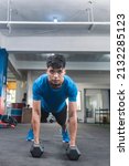 Small photo of A young man looking intensely at the camera while training at the gym. Preparing to do Renegade rows or pushup variation with hex dumbbells.