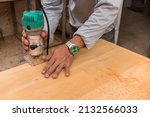 Small photo of A carpenter uses a wood trimmer to chamfer to edge of a table. Compact Wood Palm Router Tool. At a furniture making workshop.