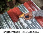 Small photo of Painting the surface of a sheet of Galvanized Iron or GI corrugated metal with rust inhibiting red oxide primer.