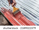 Small photo of Painting the surface of a sheet of Galvanized Iron or GI corrugated metal with rust inhibiting red oxide primer.