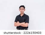 Small photo of A stern young man with his arms crossed. A supervisor in a black polo shirt and khakis. Isolated on a white background.