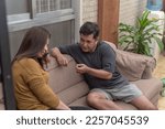Small photo of An asian woman is disappointed at her tone-deaf and childish husband lecturing her on something while sitting on the couch. Classic example of mansplaining.