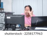 Small photo of A tired man at the office rubs his eyes while doing some menial tasks on the computer. Eyestrain and fatigue setting in.
