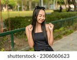 Small photo of A pretty young asian lady standing in the park feeling optimistic and giddy. Outdoor park scene.