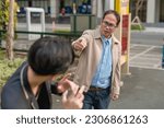 Small photo of A furious asian man confronts and corners a frightened guy in public during a chance encounter. Accusing someone of cheating, theft or other grievances.