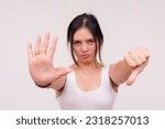 Small photo of An infuriated and serious young Asian woman doing a stop gesture on one hand and a thumbs down on the other. Isolated on a white background.