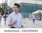 Small photo of A handsome and composed asian man in his early 20s pumps his fists after being promoted at work. An elated yet composed guy feeling vindicated outside the city plaza.