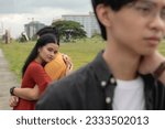 Small photo of A young woman looks back in pity at her ex-partner or rejected suitor while being embraced by her new boyfriend. A woman still having feelings for her old boyfriend while in a rebound relationship.