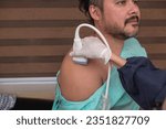 Small photo of A medical sonographer using a transducer to conduct a shoulder ultrasound of a male patient at a clinic. Checking for any rotator cuff tears.