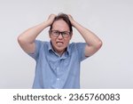 Small photo of A furious and livid middle aged asian man pulling his hair in pure rage. Going amok after being stressed out. Isolated on a white backdrop.