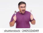 Small photo of A hungry middle aged man holding a spoon and fork looking forward with gusto to his mouthwatering meal. Ready to eat a bunch of food. Isolated on a white background.