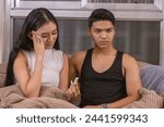 Small photo of An early-twenties Asian couple looks distressed upon finding out an unplanned pregnancy with a test kit while sitting on their living room sofa.
