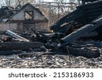 Small photo of A wooden house in the village burned down because of a forest fire. Charred boards and various things lie on the ground, covered with ash and smoke.