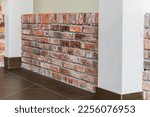 Small photo of Detail of the corner baseboard on the wall and granite tiles on the floor. The wall is lined with decorative bricks, white columns and brown baseboards. Interior design in an office building.