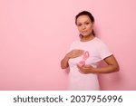 Mixed race woman puts hands around pink ribbon on her pink T Shirt, for breast cancer campaign, supporting Breast Cancer Awareness. Concept of 1 st October Pink Month and women