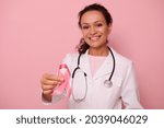 Beautiful African American female doctor with beautiful toothy smile showing a Pink satin Ribbon, isolated on colored background with copy space. World Day of fight Breast Cancer, 1 st October concept