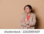 Small photo of Multi-ethnic middle aged unsure woman with folded hands, looking away, apprehensive, expressing insecurity, worry and anxiety due to lack of employment, unemployment, over beige background. Copy space