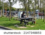 Small photo of Drongen, Oost-Vlaanderen Belgium - April 18, 2022: Adult caucasian man thirties eating a meal from Burger King on an outdoor pick nick table near parking lot highway
