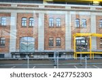 Small photo of Ostend, West-Flanders, Belgium - February 17, 2024: Entrepot-Stapelhuis shooting from inside a tram shiny windshield on a red brick bonded warehouse with yellow steel roof structure