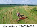 Small photo of A red tractor rakes the mown grass for drying. Modern equipment on the field. Preparations of fodder grasses for hay. Top view.